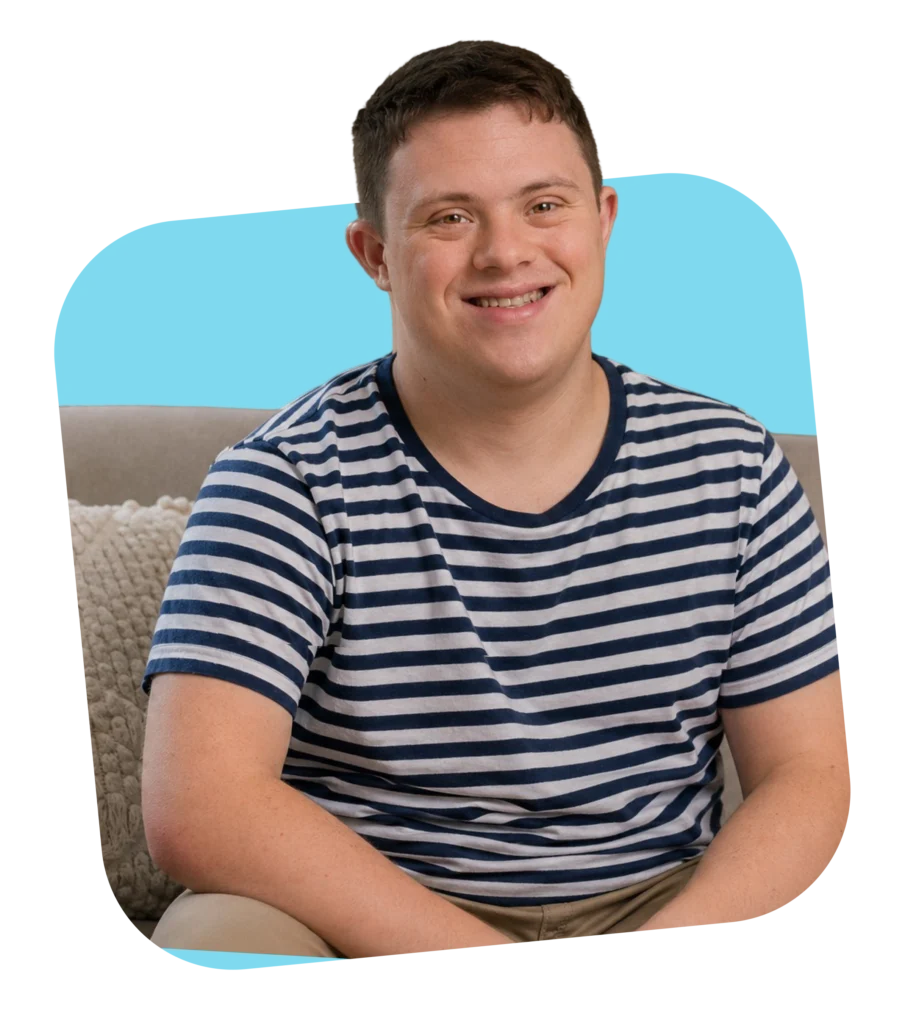 Young man with Down syndrome smiling indoors, an NDIS participant supported by Ozzy Support Mates